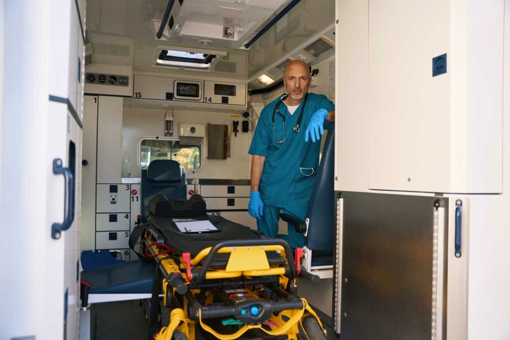 Bild von einem Krankenwagen. Im laderaum steht ein Sanitäter und schaut heraus.